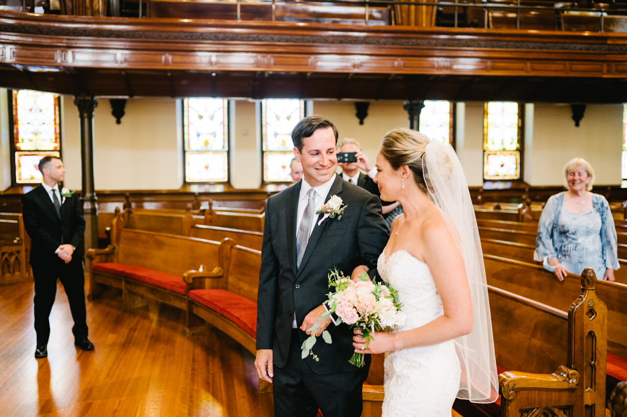  Bride and groom link arms with a smile inside first presbyterian church in portland 