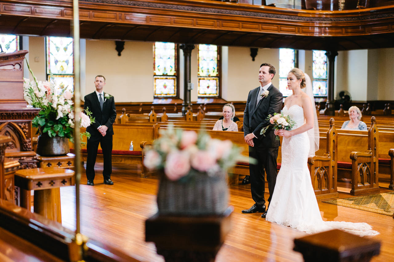  Wedding couple listens to sermon with flowers in the foreground 