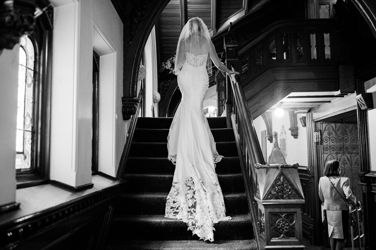  Long bride lace dress train as she walks up church stairs 