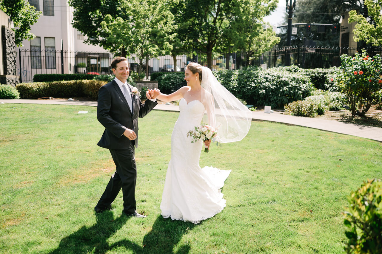  Groom laughs after spinning bride around in green church courtyard 