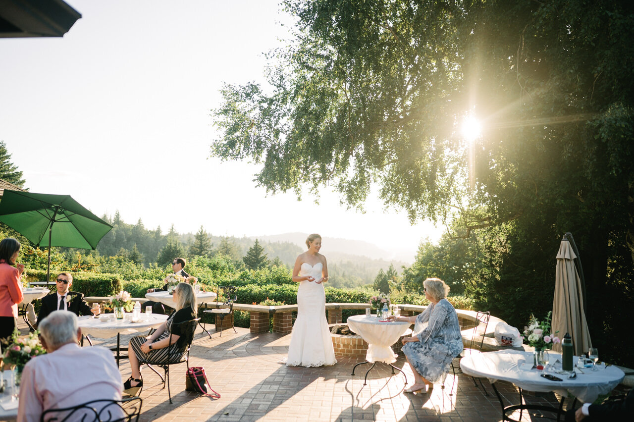  Bride stands in back patio small wedding reception with sunlight shining through trees 