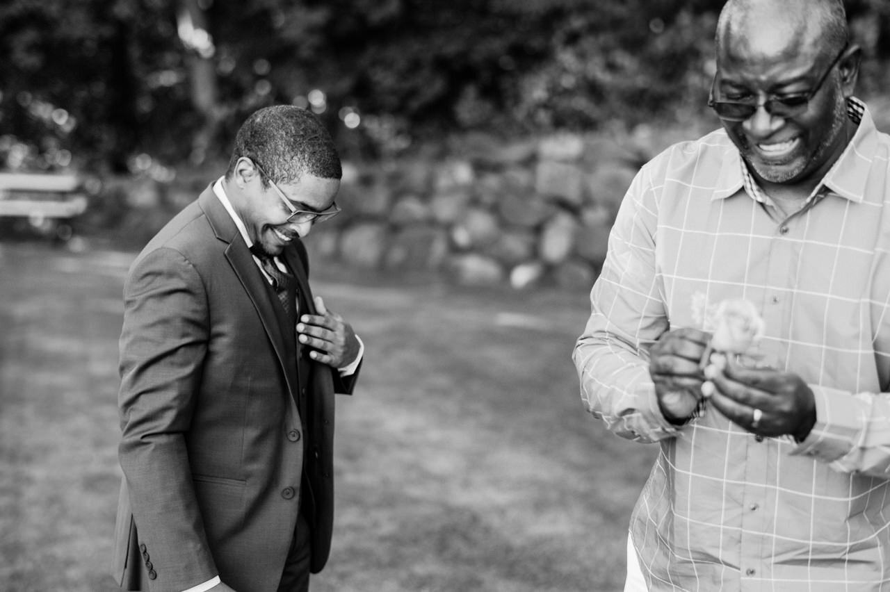  Groom laughs with father as they attempt to put on the boutonnière 