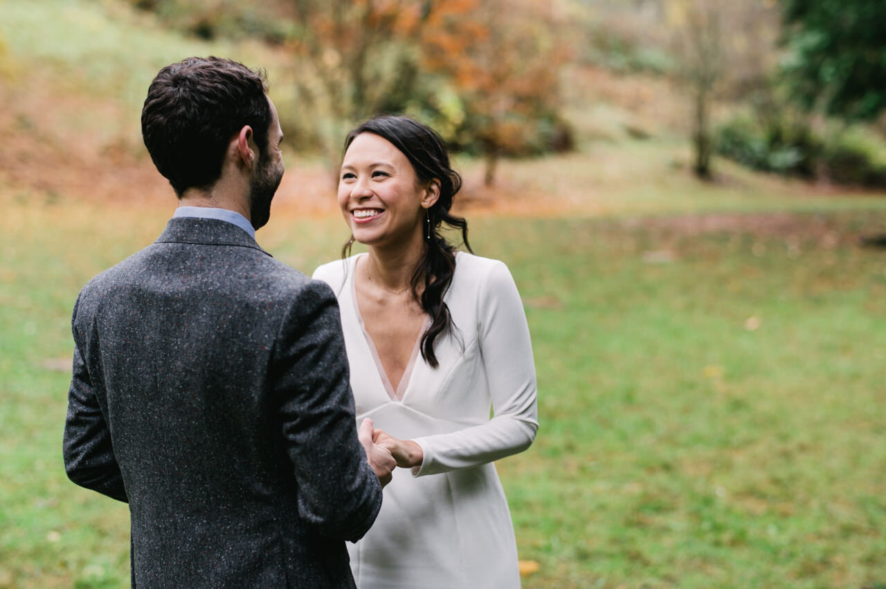  Bride with dark hair smiles at groom, holding his hand in fall first look moment 