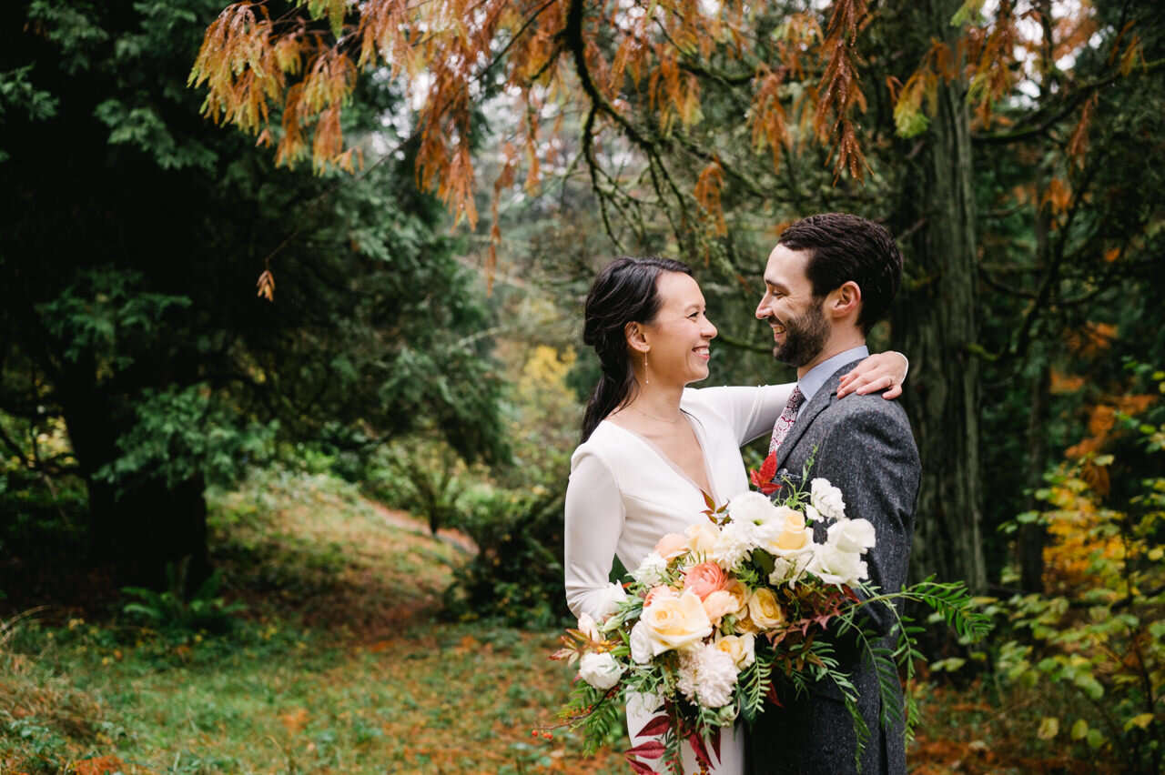  Bride and groom wrap arms around each other in fall forest scene 