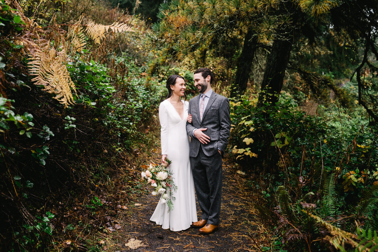  Bride and groom smile at each other while standing on hiking trail in portland forest 