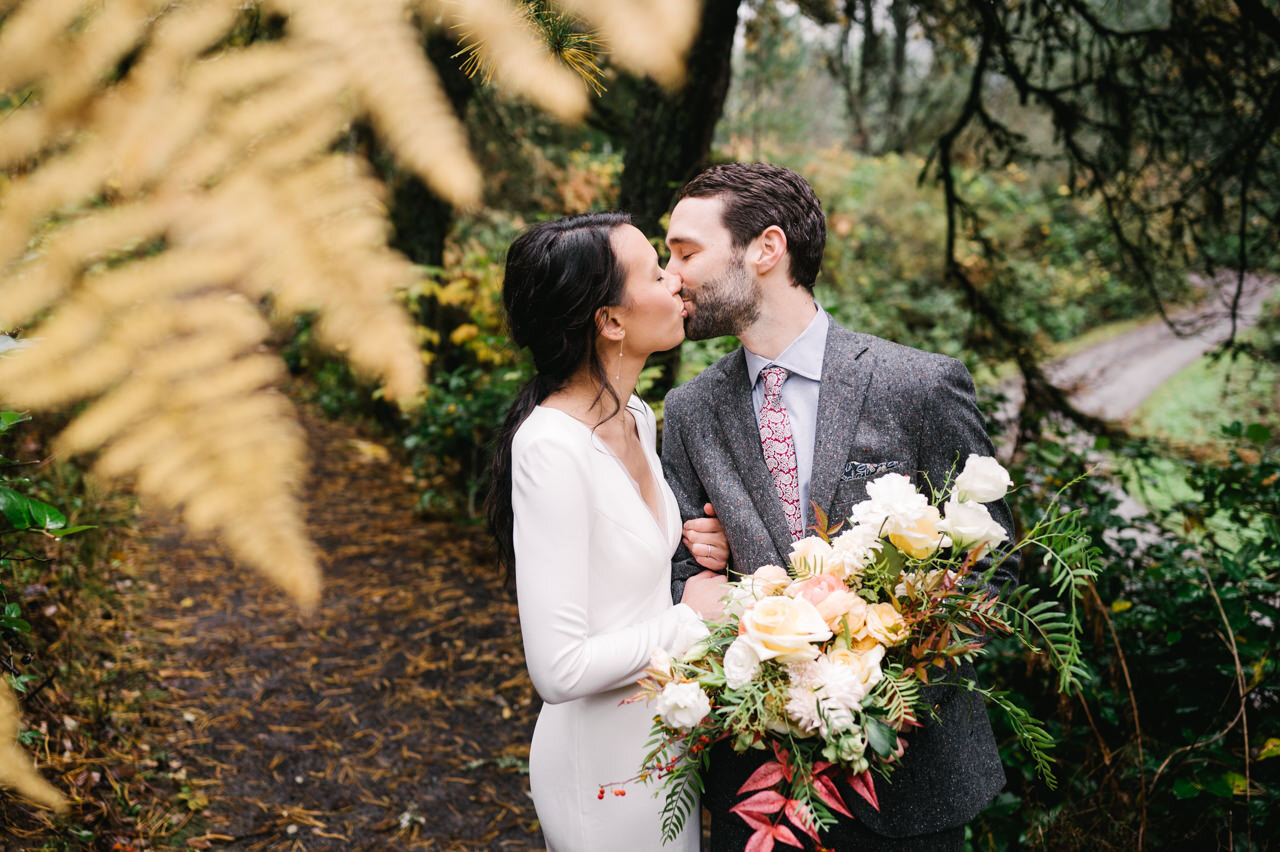  Groom kisses bride under orange fern leave on forest trail 