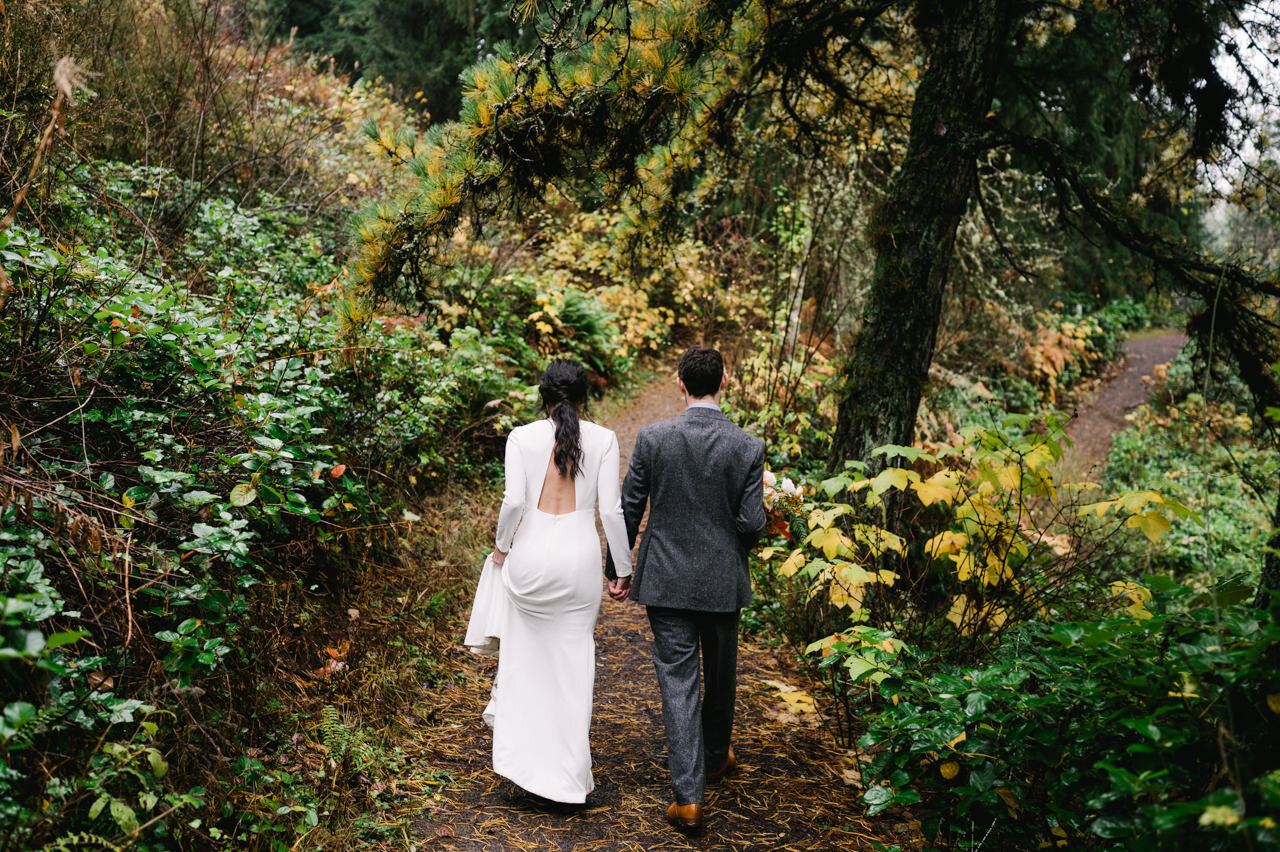 Holding hands, bride and groom walk away down hiking trail in forest park 