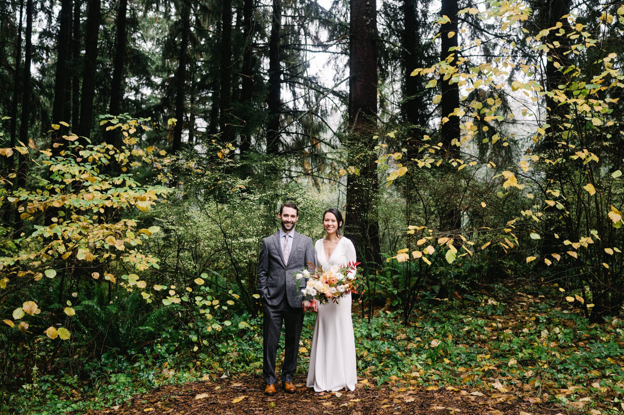 Far away portrait of bride and groom standing in yellow and green leaf forest 