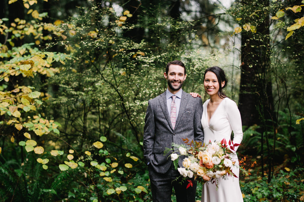  Smiling bride and groom with forest evergreens and yellow leaves surrounding them 