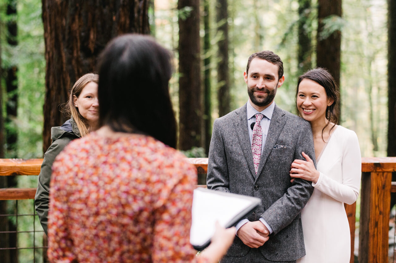  Bride and groom smiling at ceremony reading on redwood deck 