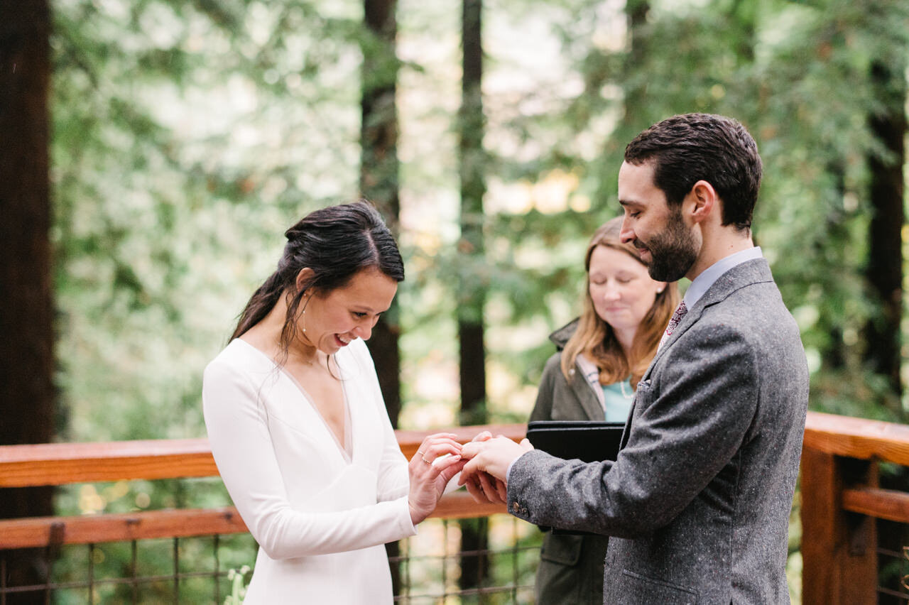  Bride places ring on groom's finger during ceremony on redwood deck in portland 