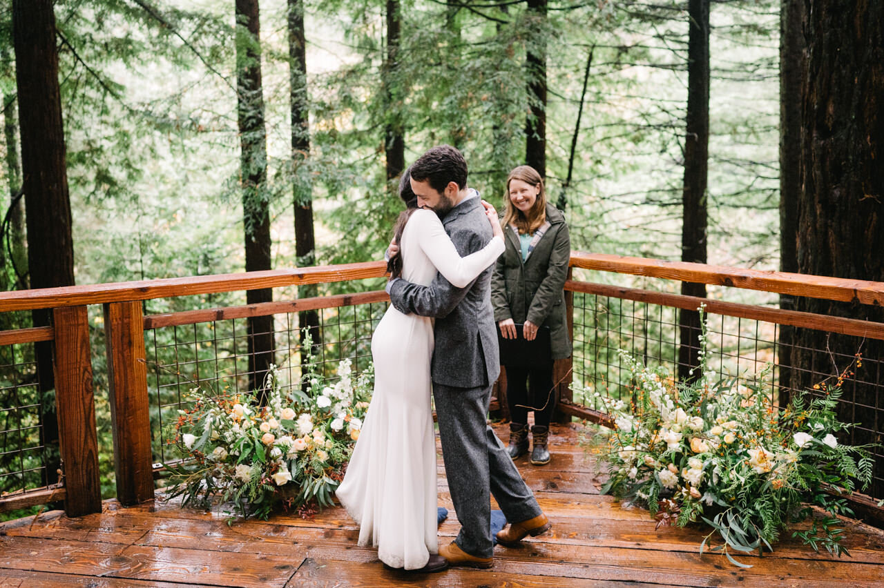  Bride and groom embrace on redwood deck in portland rain. 