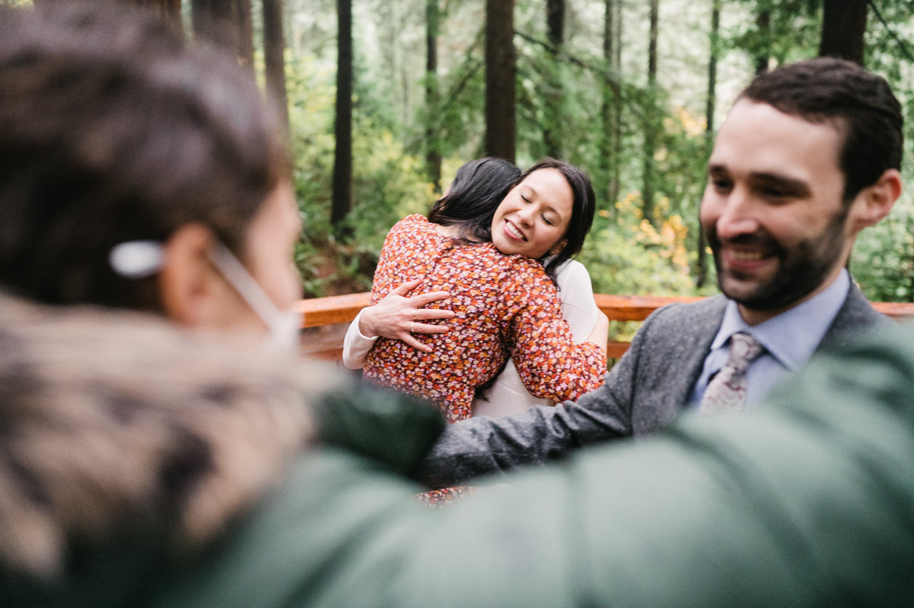  Bride hugging her sister while groom hugs guest on redwood deck in portland 