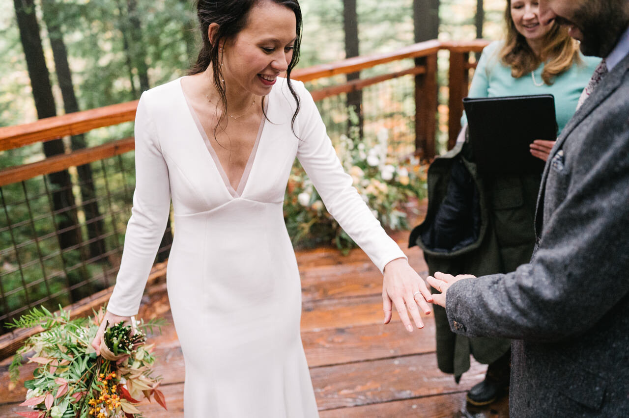  Bride shows the ring on her finger on wet redwood deck in forest 