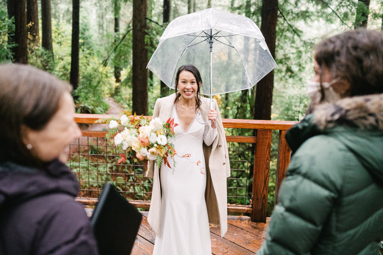  Bride showing the camera an excited face as she stands under an umbrella with her bouquet 