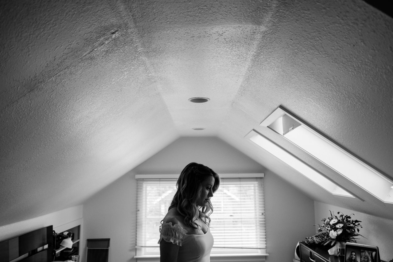  Bride stands in center of portland attic before the wedding in black and white photograph 