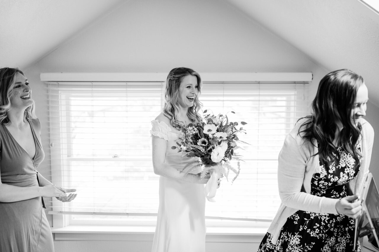  Bride in attic with bridesmaids laughs in black and white 