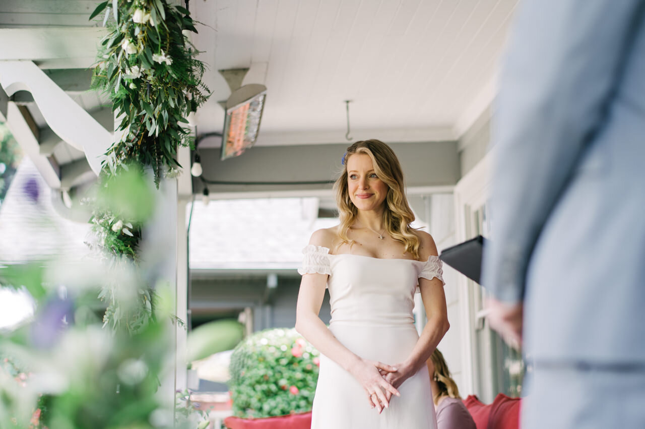  Bride smiles looking off of front porch with purple and green florals decorating the banister 