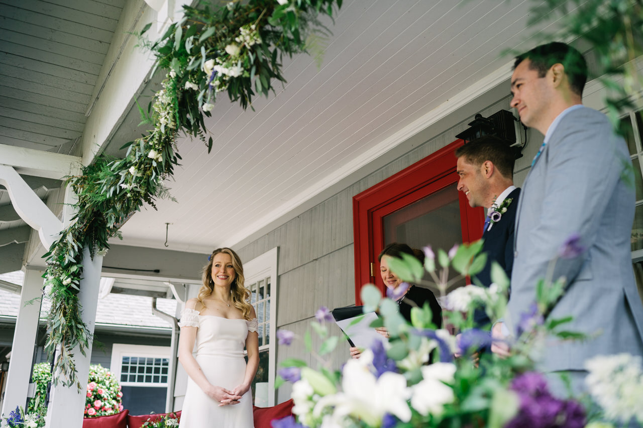  Bride smiles on front porch under florals and red door during elopement ceremony 