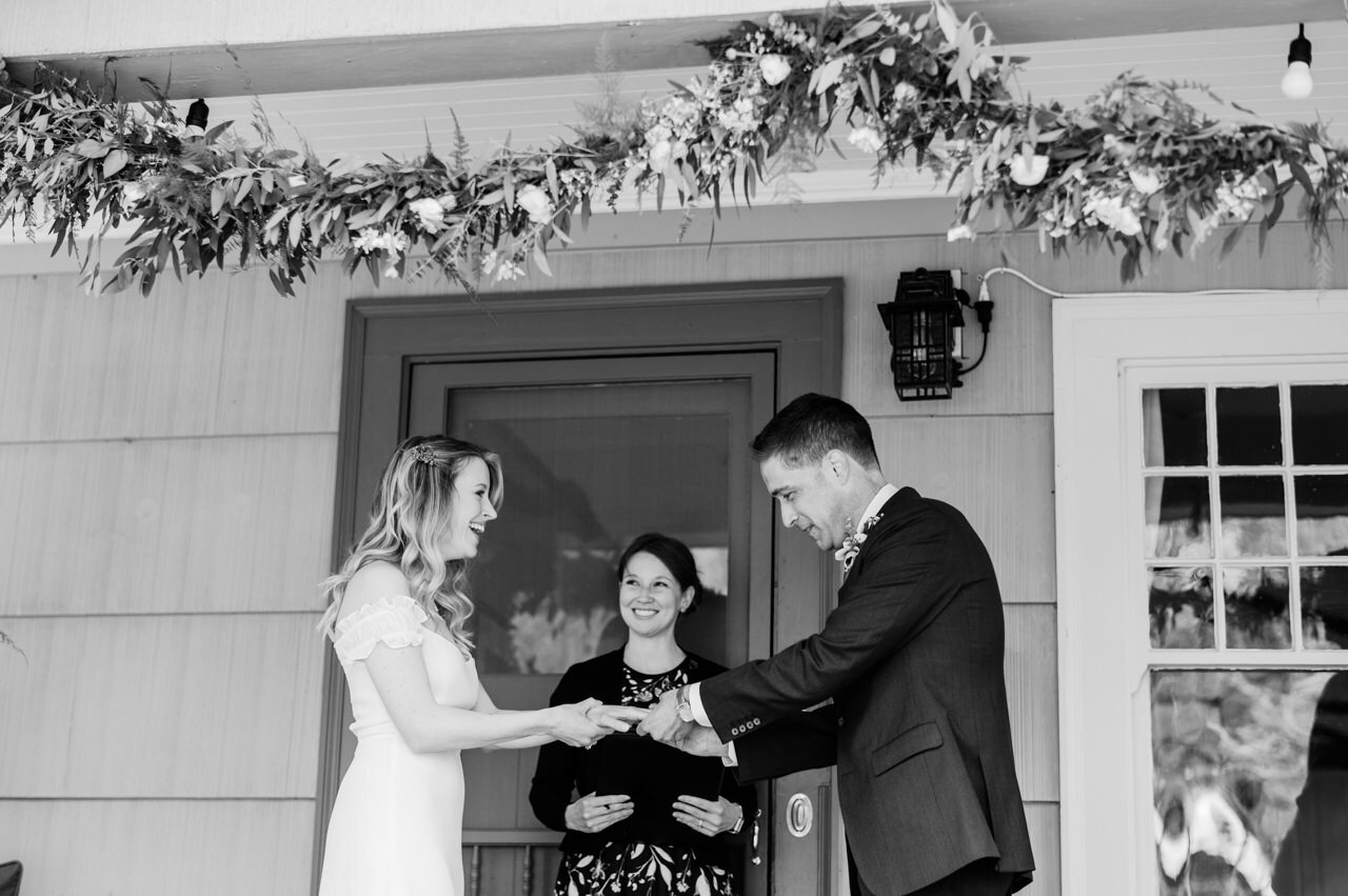  Bride smiles as groom pushes ring on finger at home elopement ceremony 