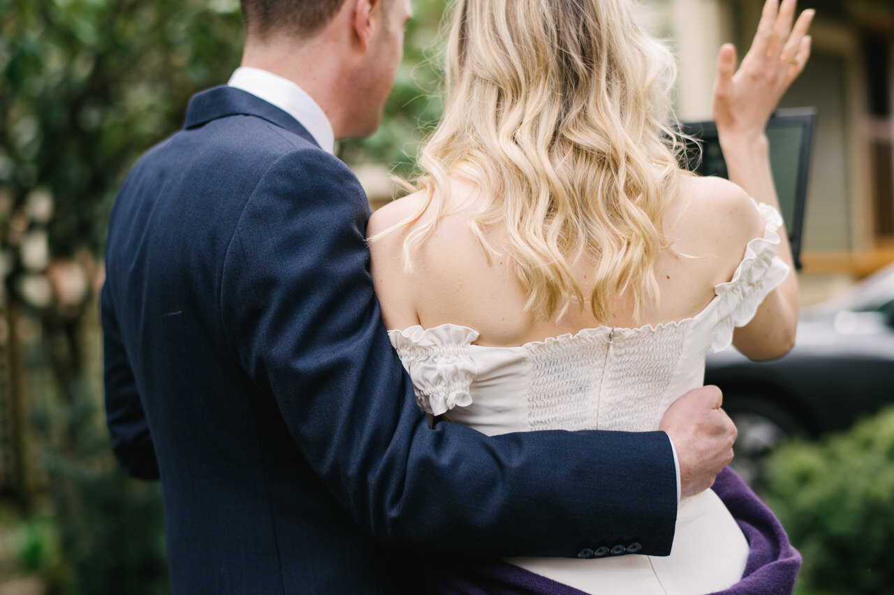  Groom wraps arm around bride from behind while blonde bride waives 