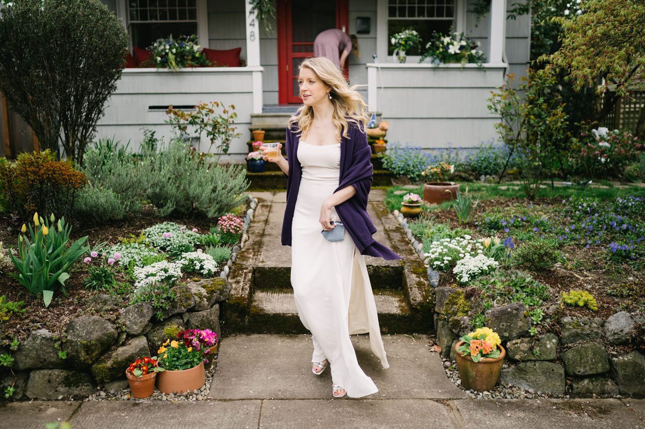  Bride with blonde hair and purple shawl walks with drink off front porch at elopement 