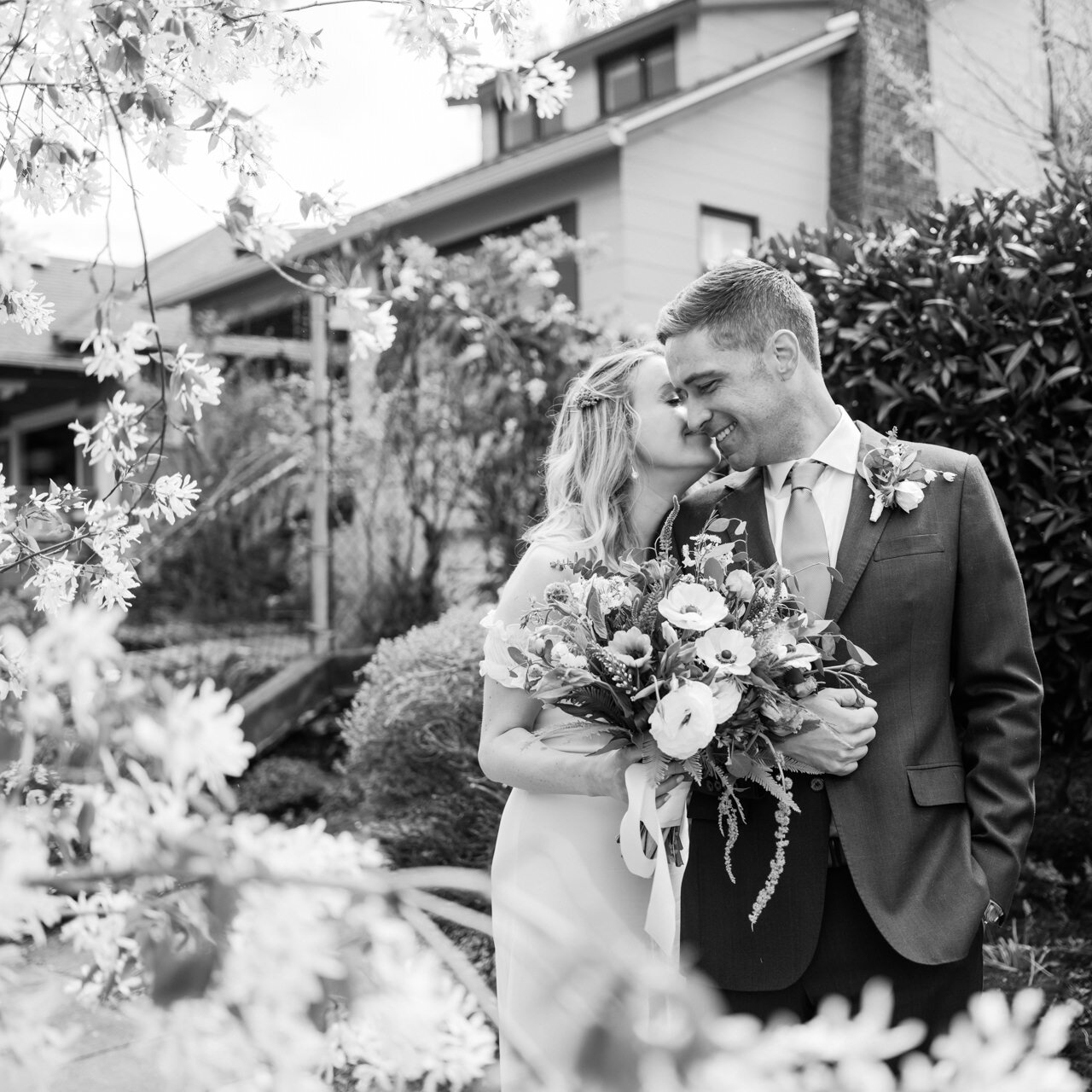  Square portrait of bride kissing groom's cheek in black and white 