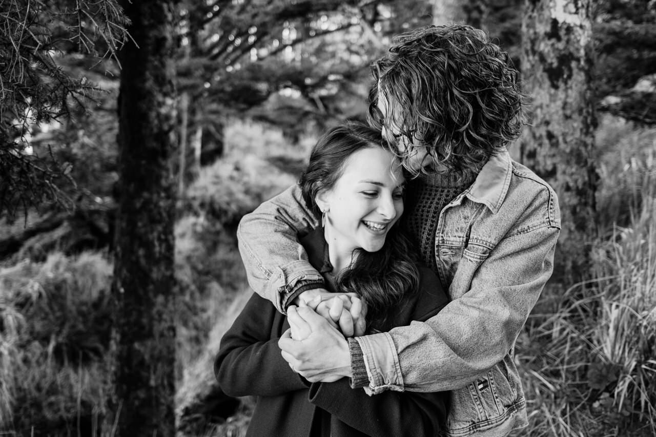  Girl smiles while boy in jean jacket embraces her from behind 