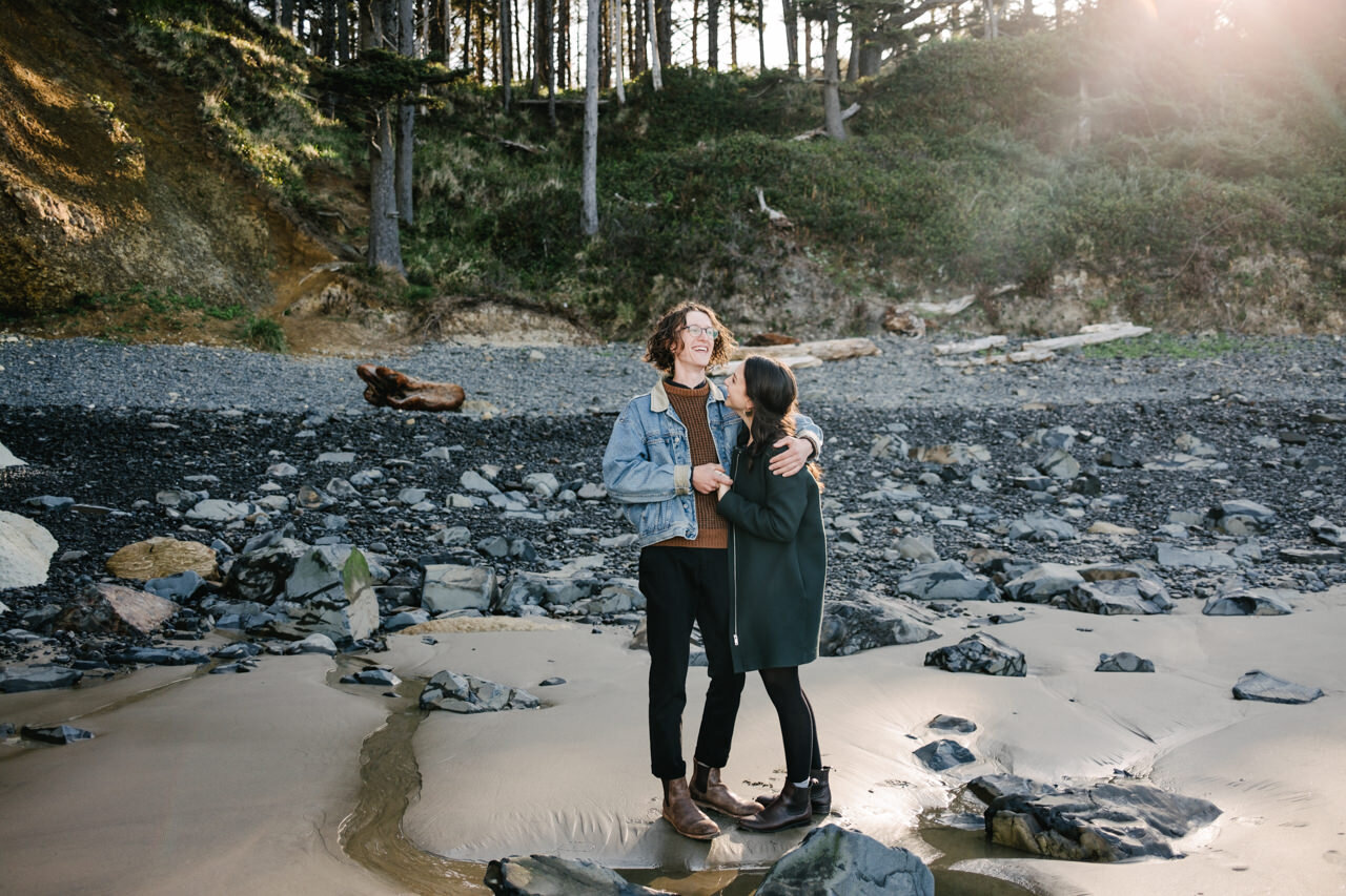  Engaged couple stands on sand and rocks on Oregon coast while boy smiles 