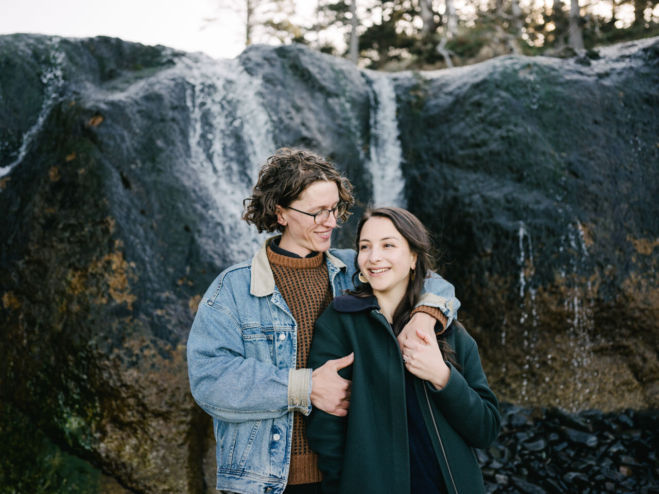  Girl laughs holding hand of fiancé in front of hug point waterfall 