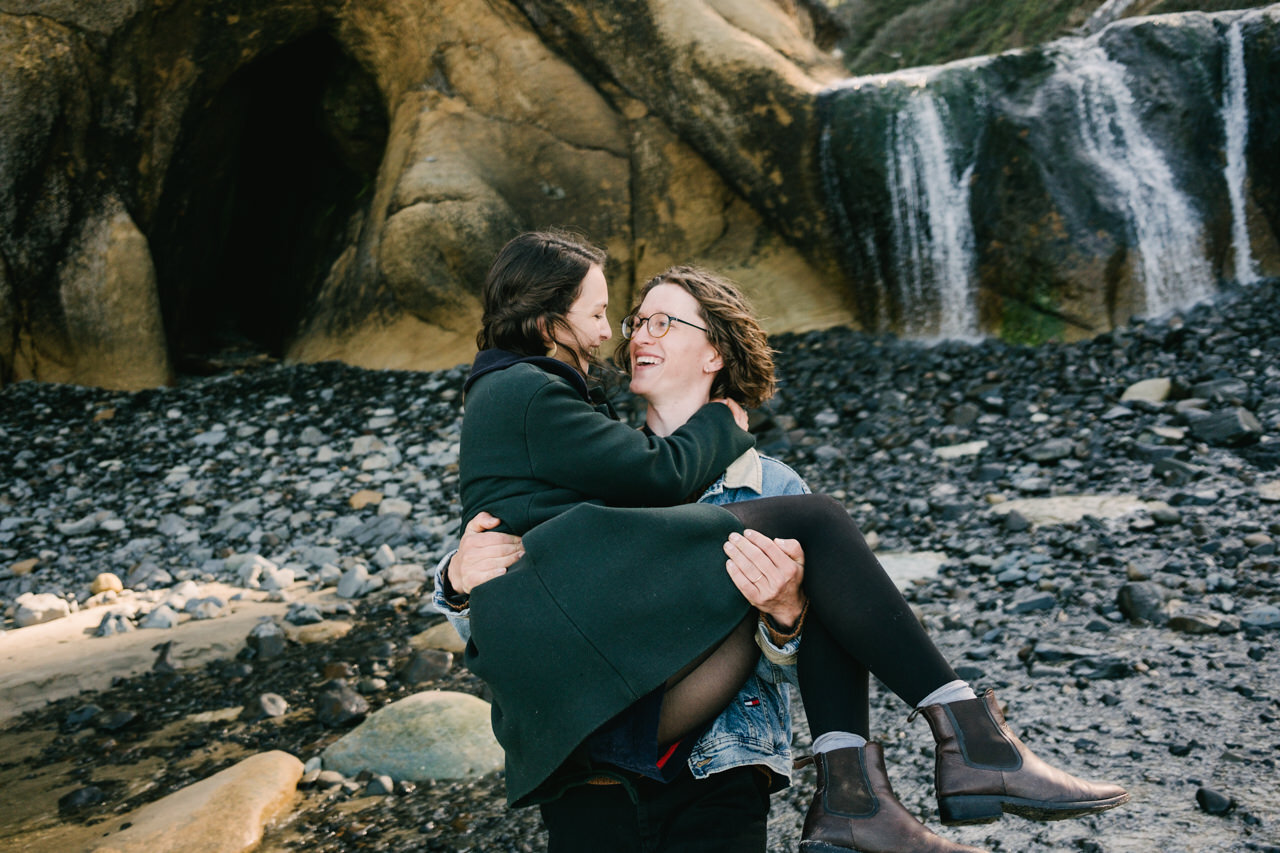  Boy holding girl in front of hug point waterfall and wet stones 