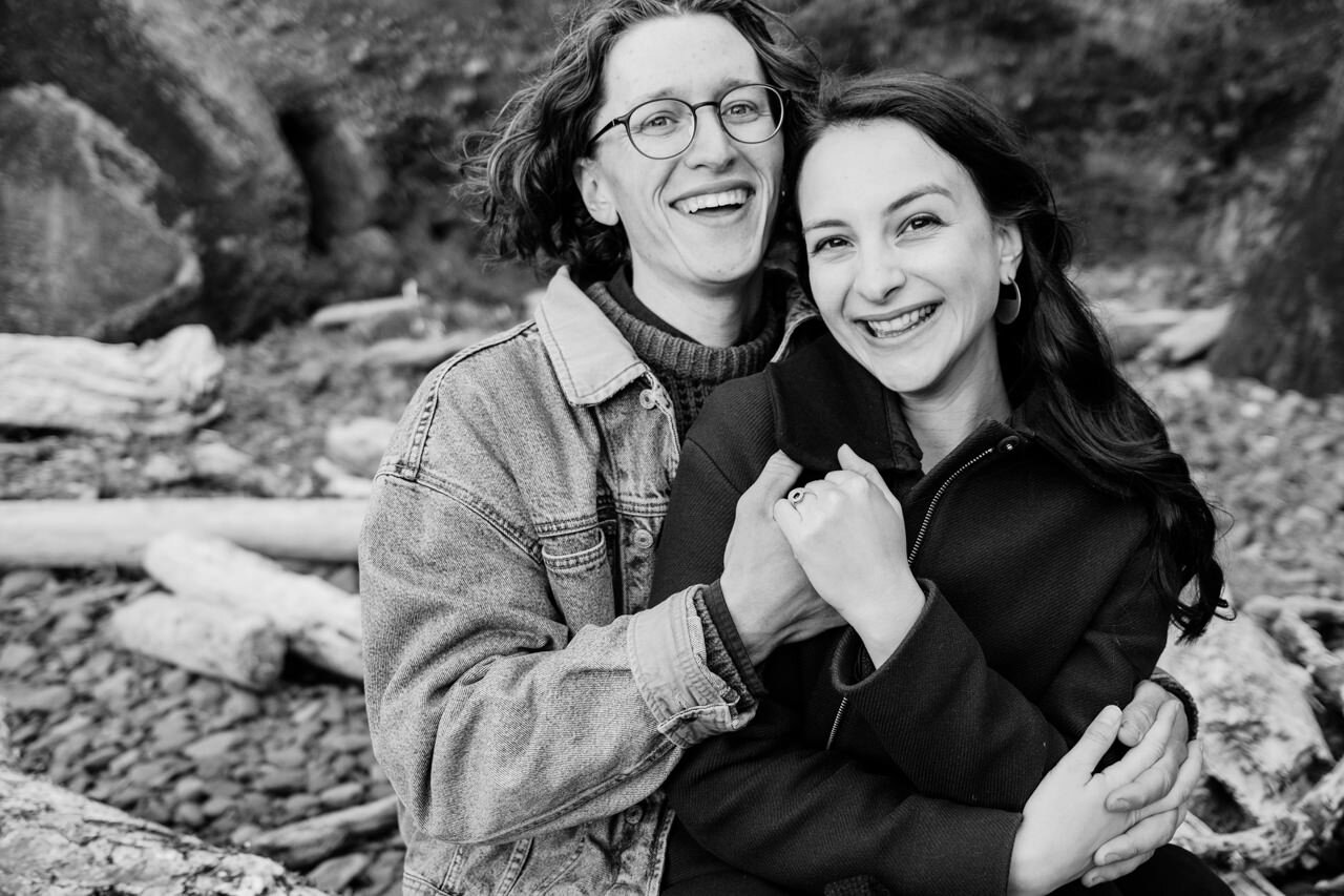  Engaged couple laughing together on Oregon coastal logs 