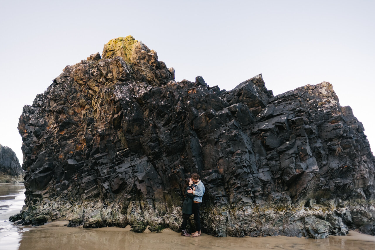  Couple snuggles in front of jagged Oregon coast rock at hug point 