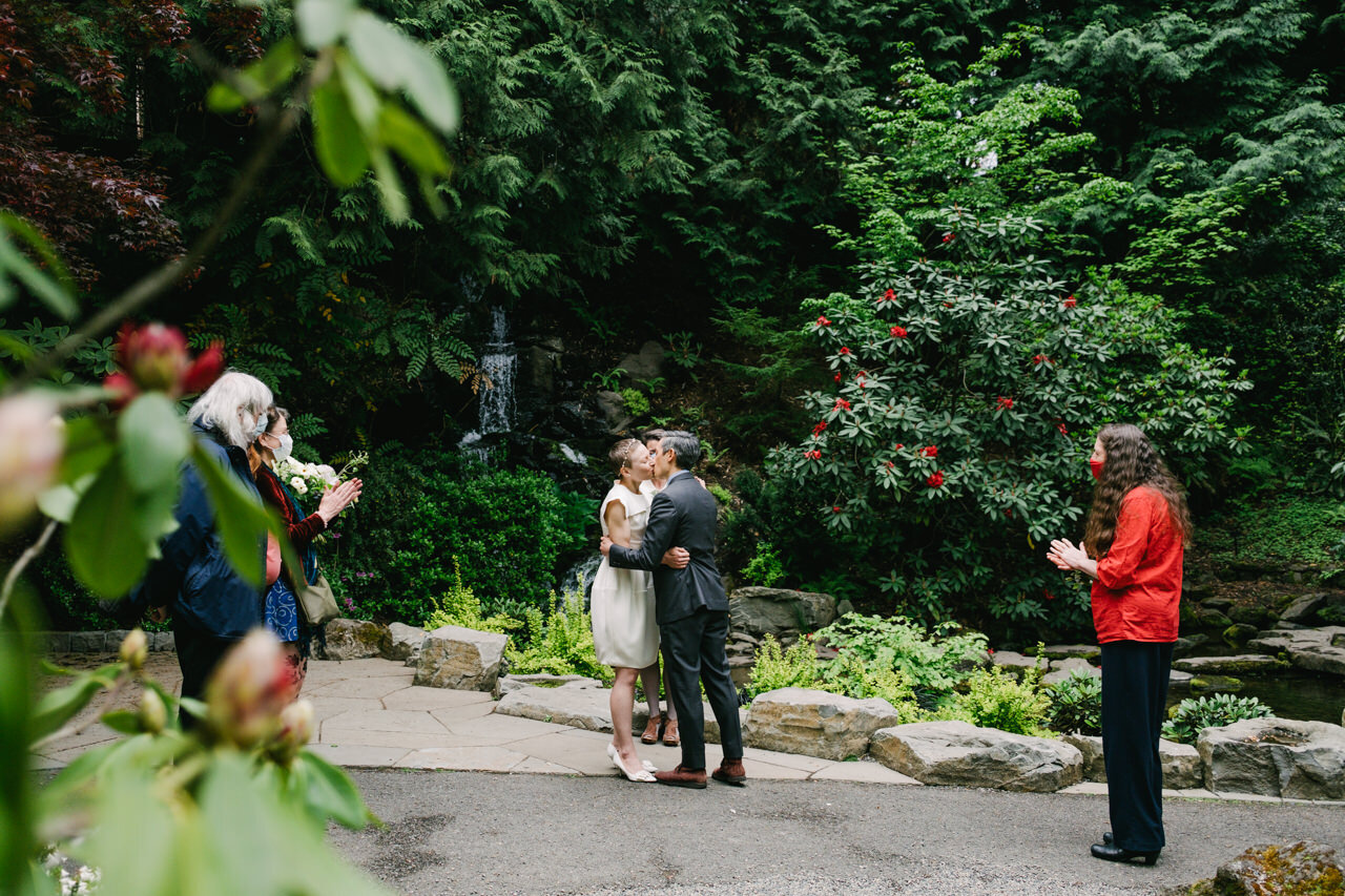  Bride and groom kiss during elopement at crystal springs in front of waterfall and red Rhododendrons 