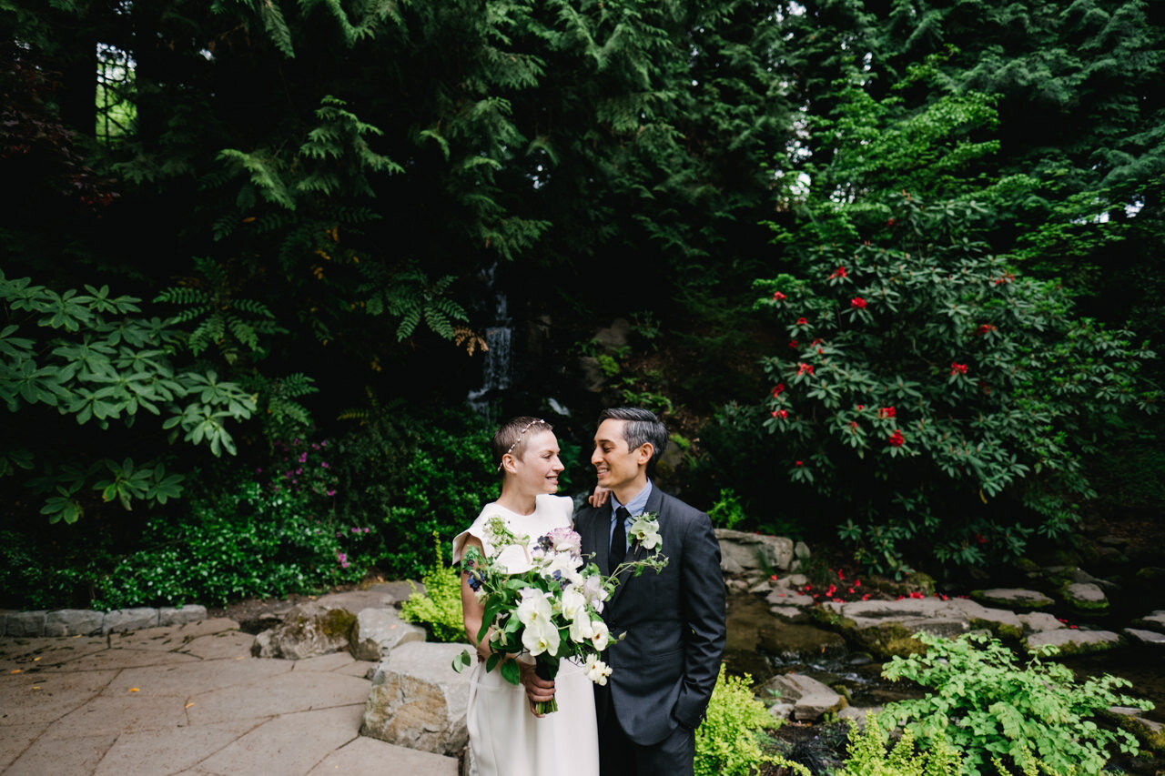  Bride and groom gaze at each other in front of waterfall and pond and rhododendrons 