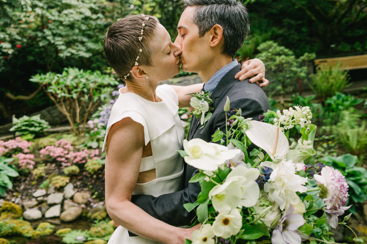 Eloped bride and groom kiss surrounded by lush crystal springs gardens with lily bouquet 
