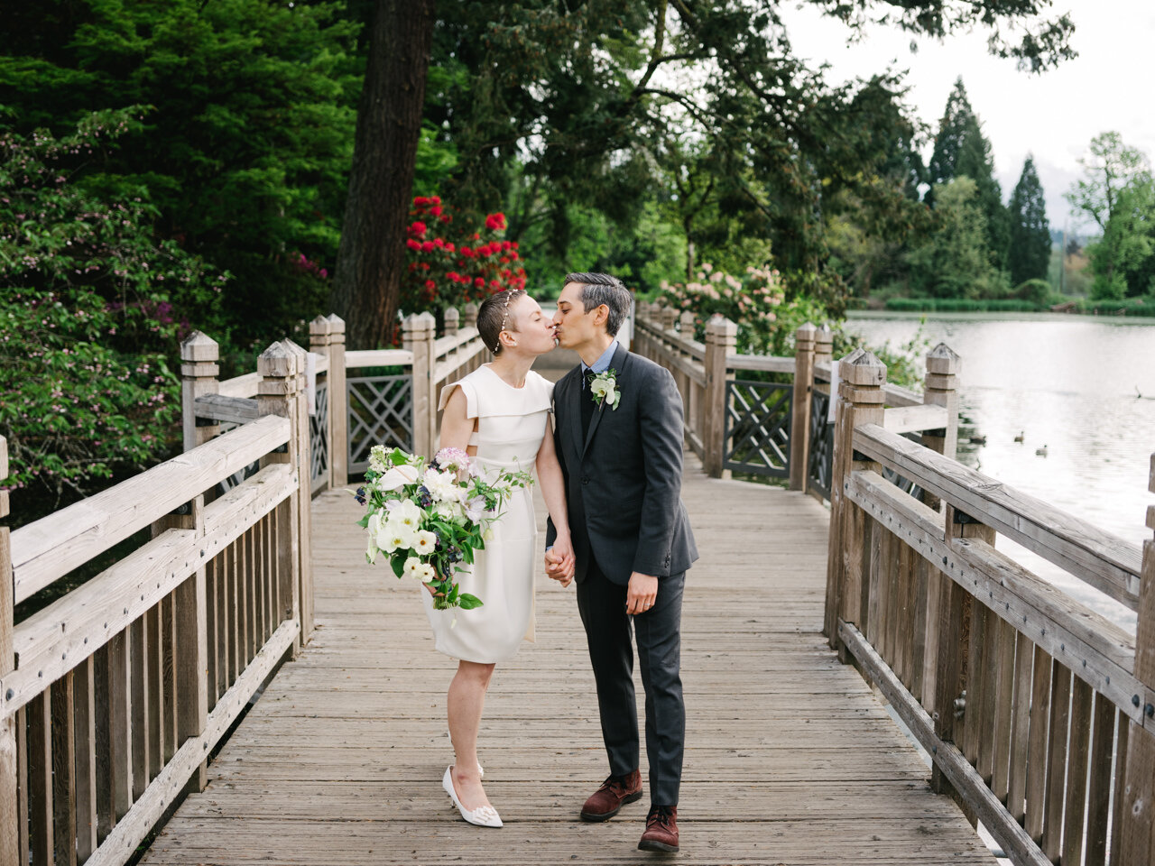  Kiss during elopement on crystal springs bridge with red rhododendrons and lake behind them 