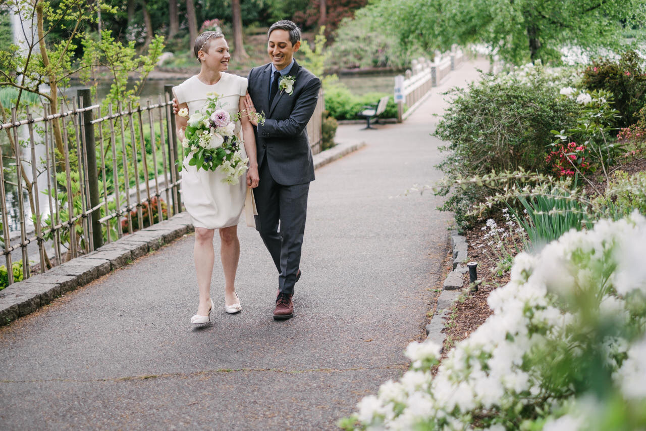  Groom holds bride's arm as they share conversation while walking crystal springs pathways 