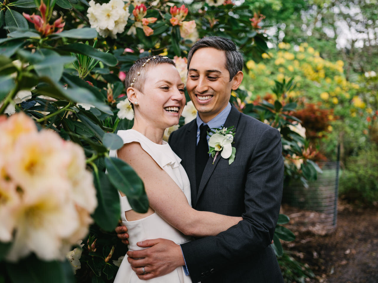  Bride laughs while snuggled with groom in yellow and red rhododendrons 