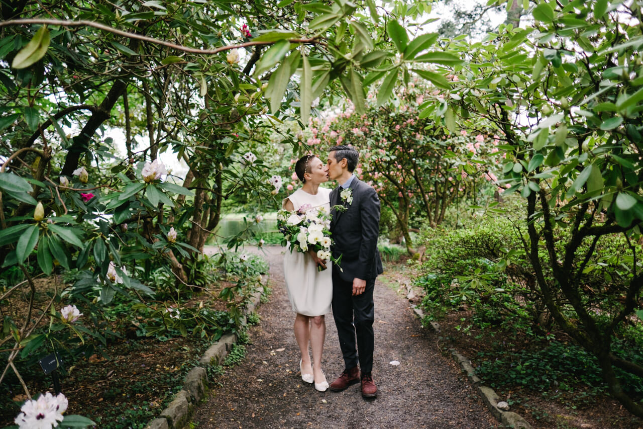  Bride and groom share a kiss walking in rhododendron path 