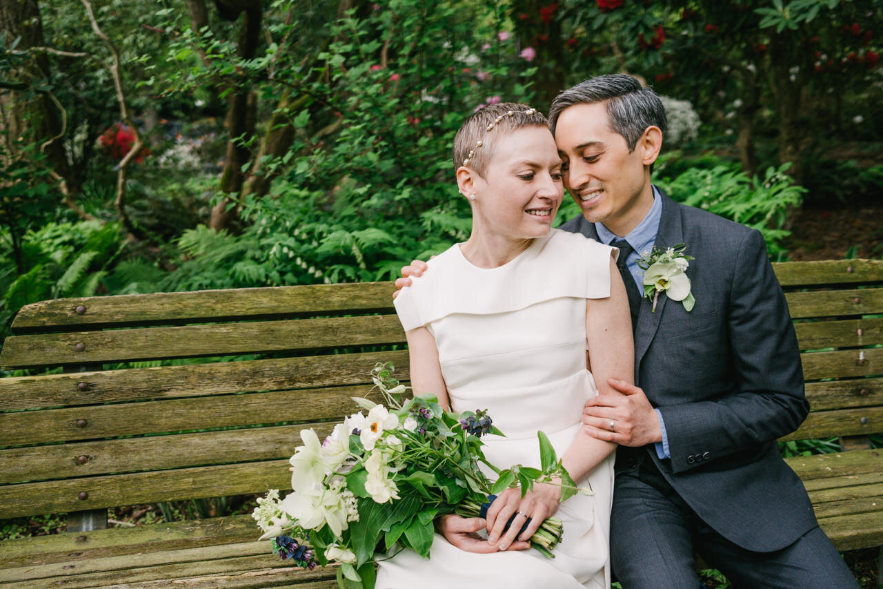  Bride in modern white dress sits on bench with groom together 