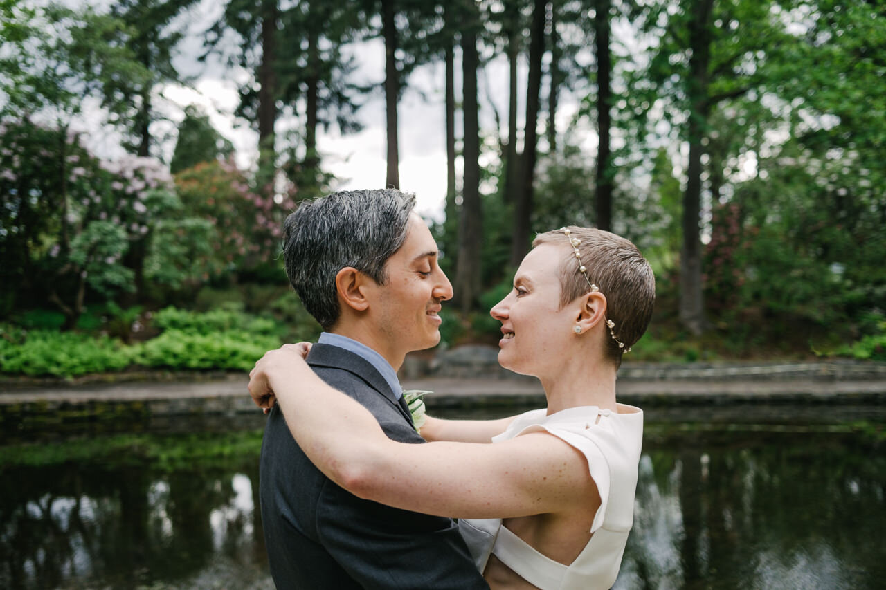  Bride and groom admire each other in front of pond and tall fir trees at crystal springs 
