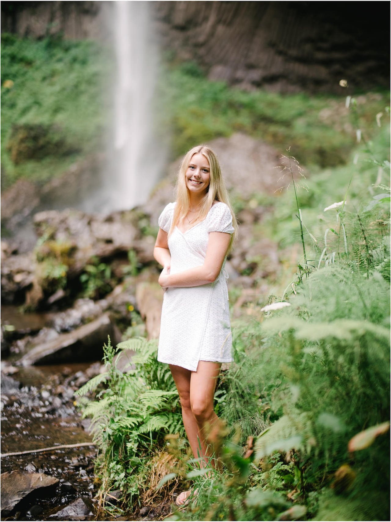  High school senior portrait of tall blonde girl leaning on hip in ferns in front of latourell falls 