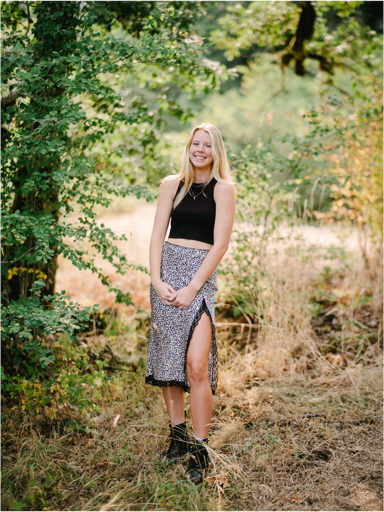  Smiling blonde senior girl in black tank top and dress with slit laughing in oak tree grove 