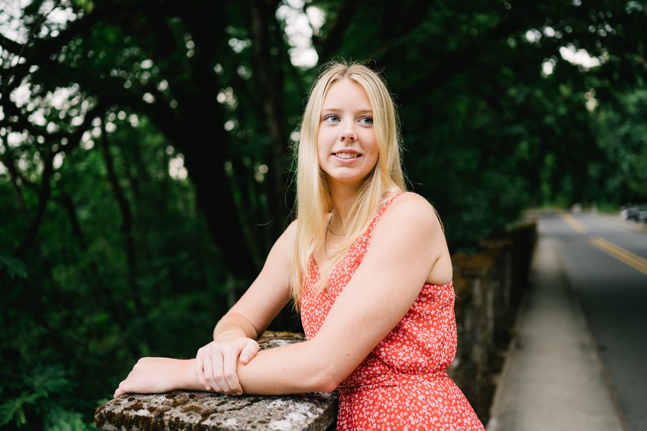  High school senior girl looks away down highway on tree lined bridge 