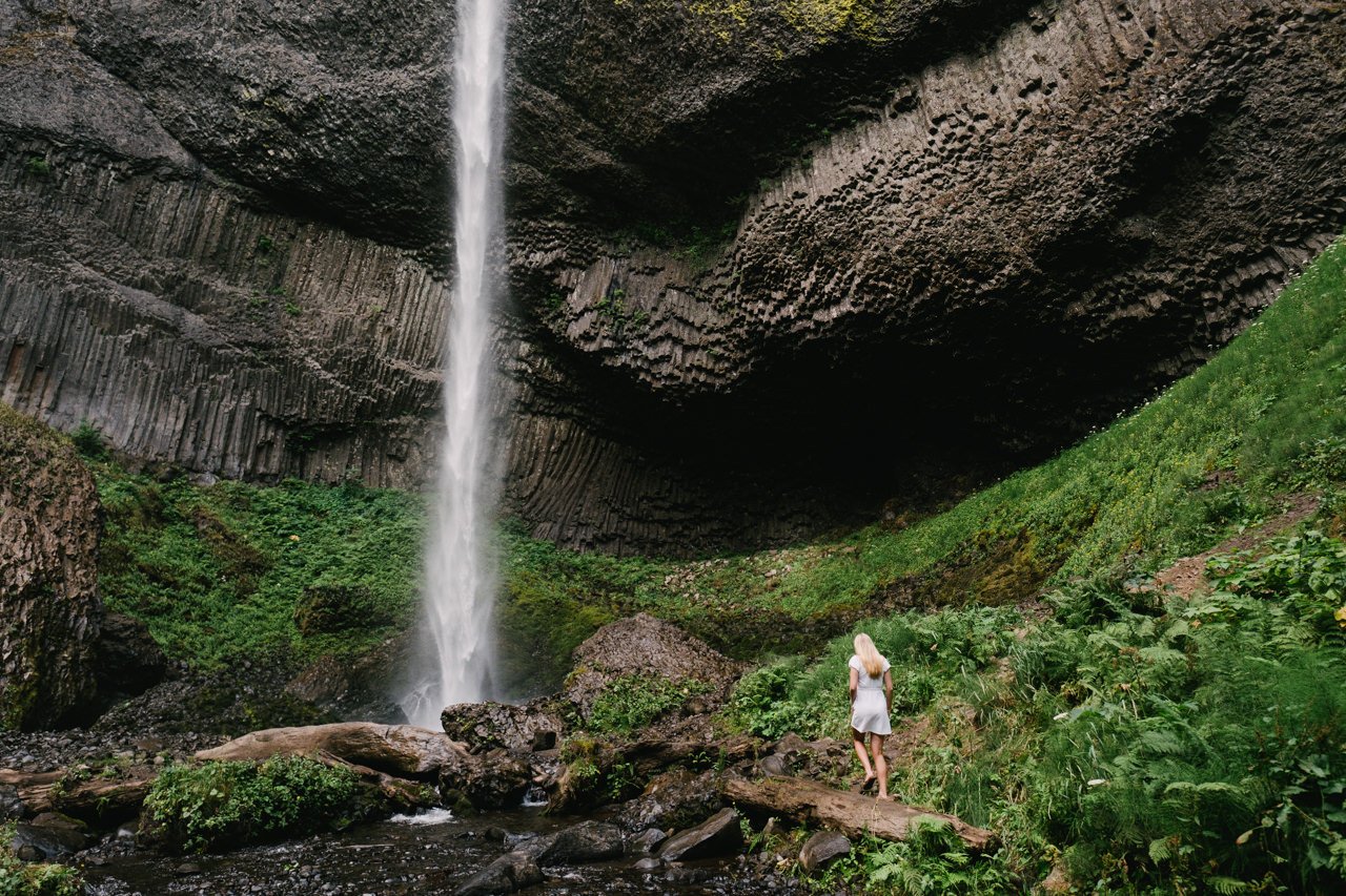  Blonde senior high school student walks toward basalt surrounded waterfall 