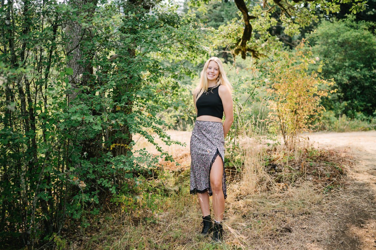  Girl in black shirt and skirt smiling in sunshine and oak trees 