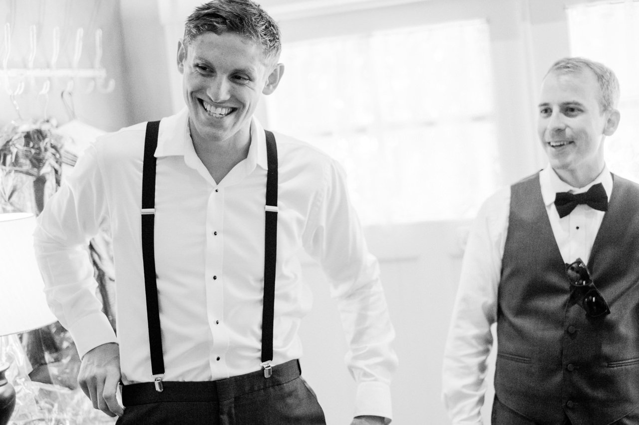  Groom laughing while getting ready in black and white candid moment 