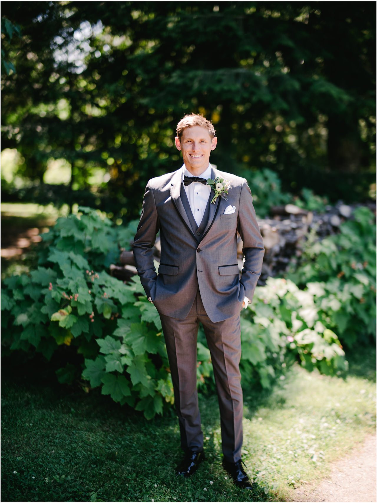  Classic groom portrait in front of wood pile surrounded by green shrubbery 