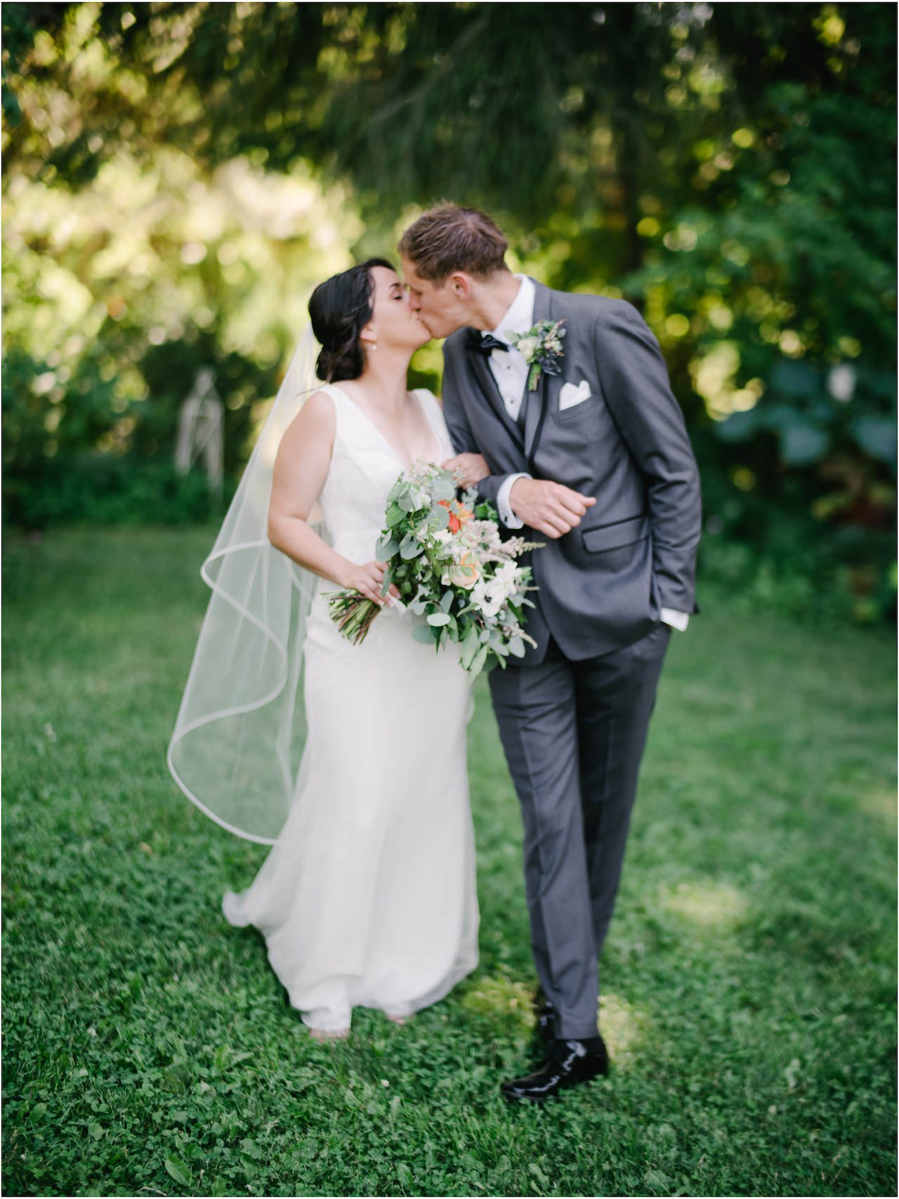  Bride and groom kiss while walking, holding orange and pink and white bouquet 